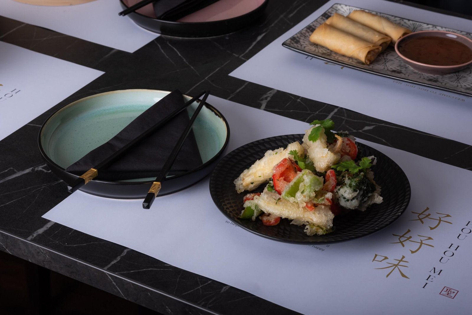 Tempura and spring rolls plated on branded Hou Hou Mei paper mats with chopsticks and dipping sauce