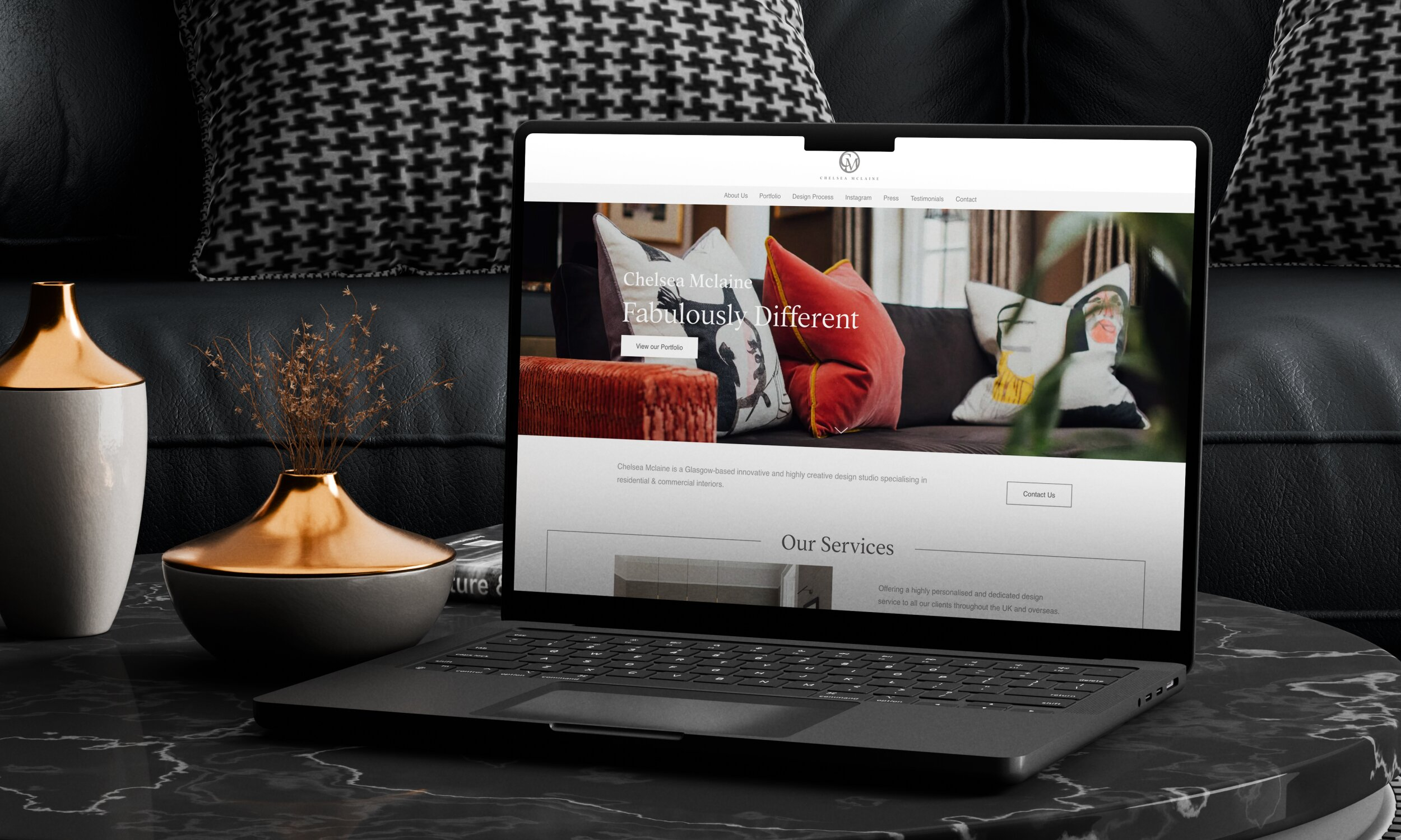 Laptop displaying Chelsea Mclaine interior design website on marble table with luxury home accessories